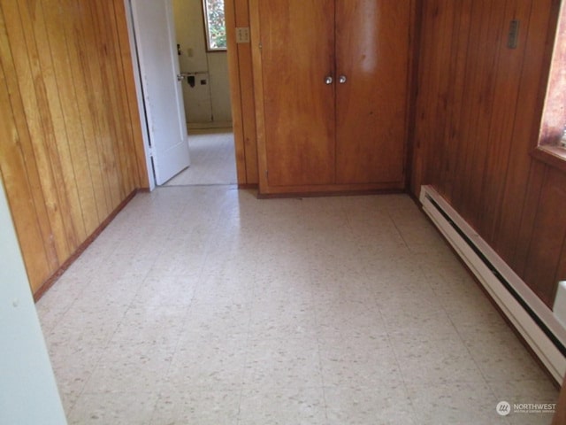 unfurnished room featuring light floors, a baseboard radiator, and wood walls