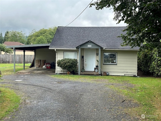 view of front of home featuring roof with shingles, fence, a carport, and driveway