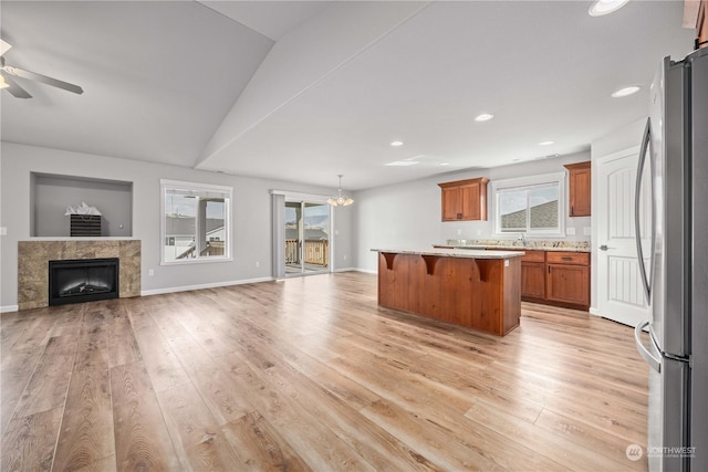 kitchen with light hardwood / wood-style flooring, stainless steel refrigerator, a kitchen bar, a fireplace, and a kitchen island