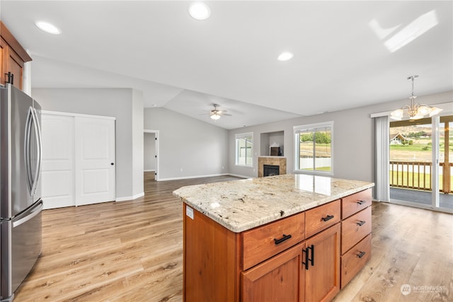 kitchen with a center island, lofted ceiling, hanging light fixtures, stainless steel fridge, and light stone counters