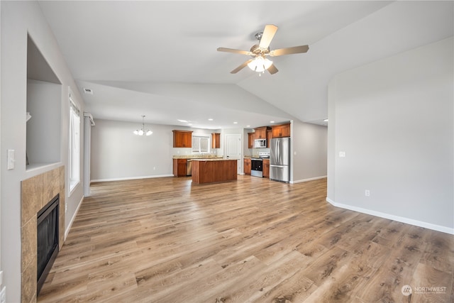 unfurnished living room with vaulted ceiling, ceiling fan with notable chandelier, a tiled fireplace, and light wood-type flooring