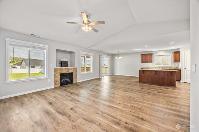 unfurnished living room featuring lofted ceiling, wood-type flooring, a fireplace, and ceiling fan with notable chandelier