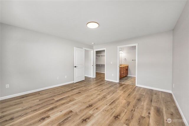 unfurnished bedroom with a spacious closet, a closet, connected bathroom, and hardwood / wood-style floors