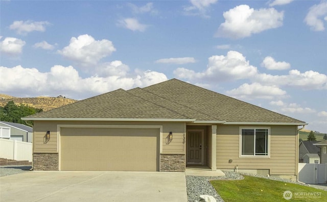 view of front facade with driveway, a shingled roof, a garage, and fence