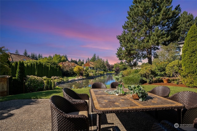 patio terrace at dusk with a water view and a yard