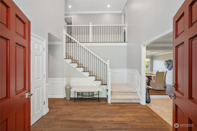 entryway with stairway, a decorative wall, wood finished floors, and ornamental molding