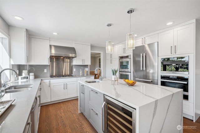 kitchen with stainless steel appliances, sink, wall chimney range hood, wine cooler, and a center island with sink