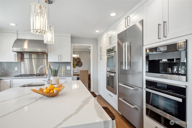 kitchen with backsplash, stainless steel appliances, dark wood-type flooring, light stone countertops, and wall chimney exhaust hood