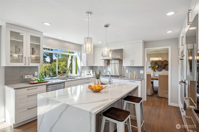 kitchen featuring light stone countertops, wall chimney exhaust hood, white cabinets, and a kitchen island with sink