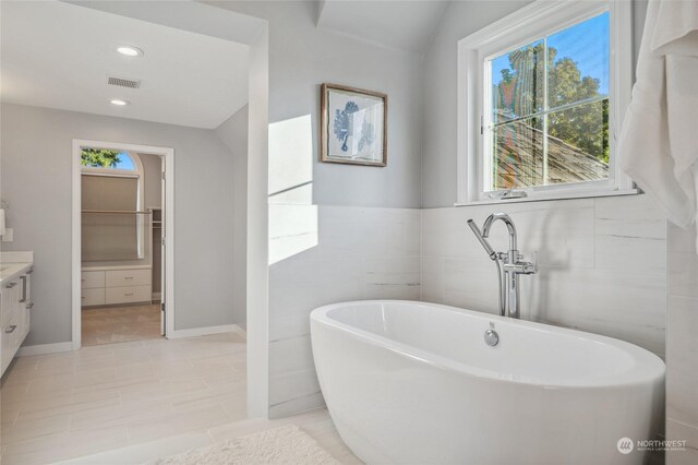 bathroom with tile patterned flooring, vanity, a bath, and tile walls