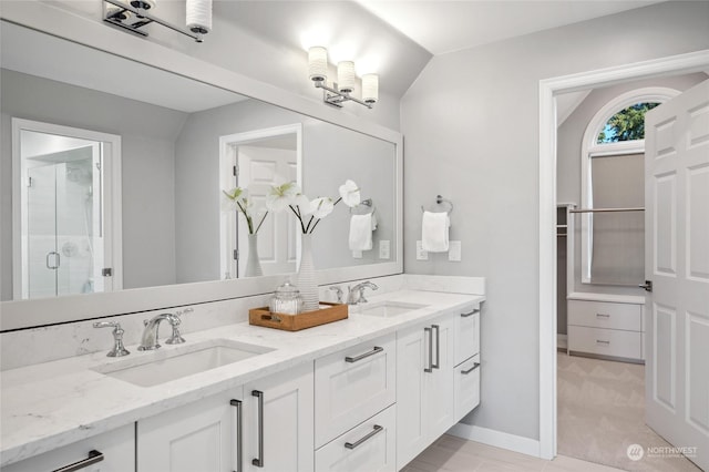 bathroom featuring a stall shower, a sink, baseboards, and double vanity