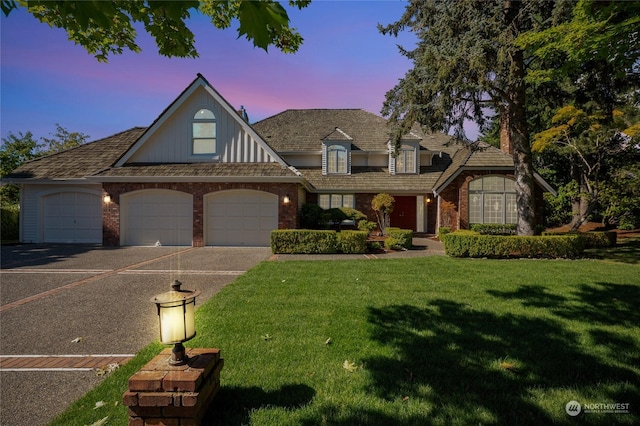 view of front facade with an attached garage, a yard, aphalt driveway, and brick siding