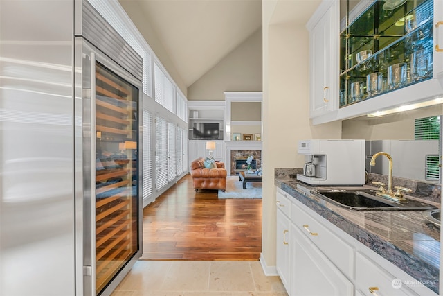 kitchen featuring light wood-type flooring, vaulted ceiling, sink, dark stone countertops, and white cabinetry