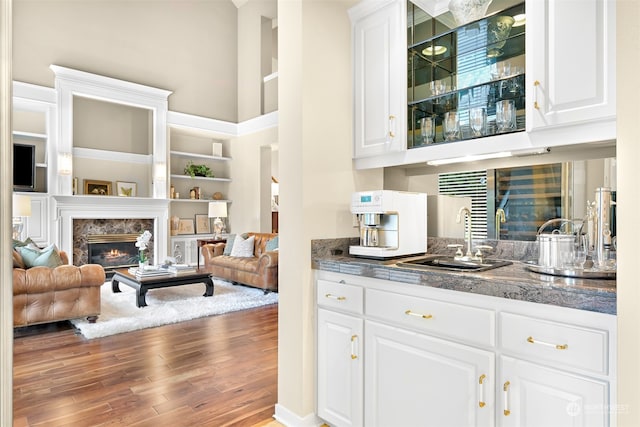 bar with a high ceiling, white cabinets, sink, hardwood / wood-style flooring, and a fireplace