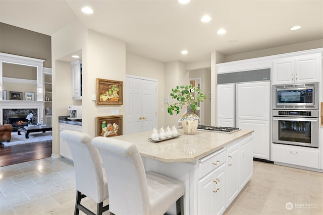 kitchen featuring a high end fireplace, light wood-type flooring, stainless steel appliances, white cabinetry, and a kitchen island