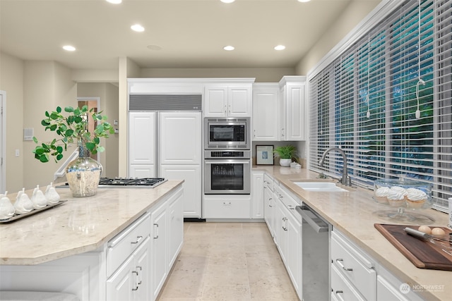 kitchen with white cabinets, built in appliances, light stone counters, and sink