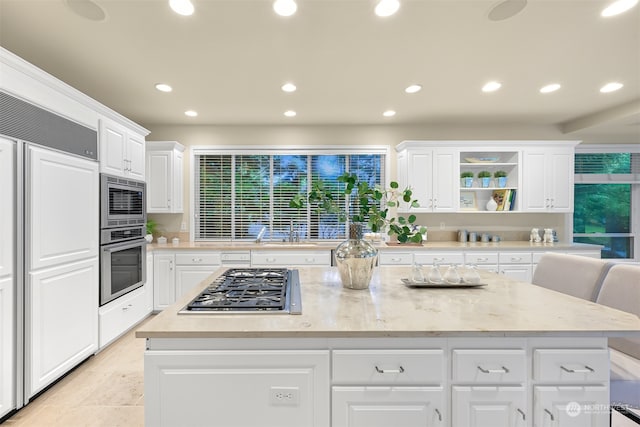 kitchen with a center island, light stone counters, light tile patterned flooring, built in appliances, and white cabinets