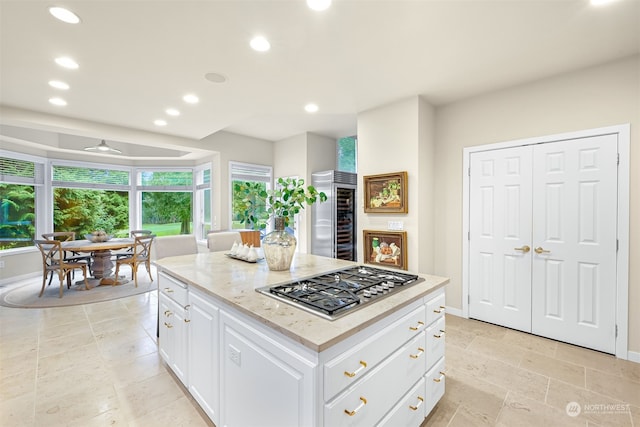 kitchen featuring ceiling fan, a center island, beverage cooler, stainless steel gas stovetop, and white cabinets