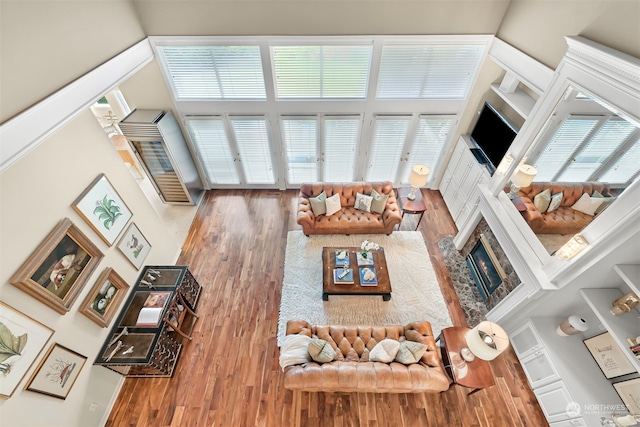 living room with a stone fireplace, wood-type flooring, and a high ceiling