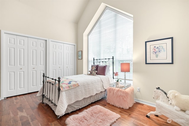 bedroom featuring hardwood / wood-style floors, lofted ceiling, multiple windows, and multiple closets