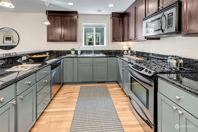 kitchen featuring dark stone counters, sink, hanging light fixtures, appliances with stainless steel finishes, and light hardwood / wood-style floors