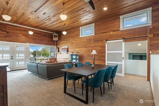 dining space with carpet, a towering ceiling, a barn door, wood ceiling, and wooden walls