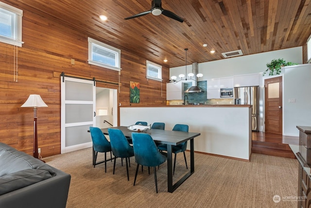 carpeted dining area with a barn door, wooden ceiling, wooden walls, visible vents, and a ceiling fan