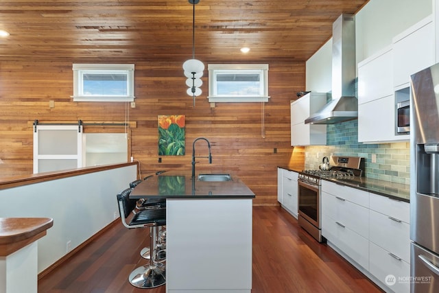 kitchen featuring a sink, appliances with stainless steel finishes, wall chimney range hood, dark countertops, and modern cabinets