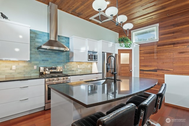 kitchen featuring dark countertops, appliances with stainless steel finishes, a sink, modern cabinets, and wall chimney exhaust hood