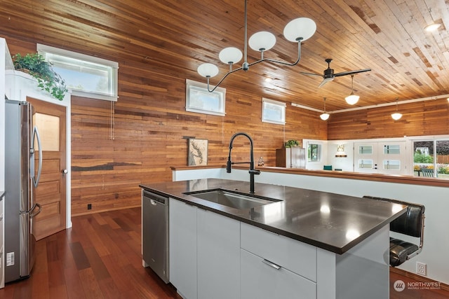 kitchen featuring white cabinets, dark countertops, appliances with stainless steel finishes, a kitchen island with sink, and a sink