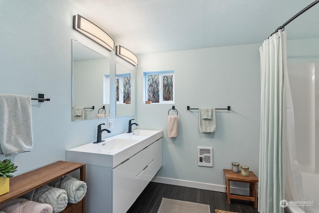 full bath featuring double vanity, wood finished floors, a sink, and baseboards