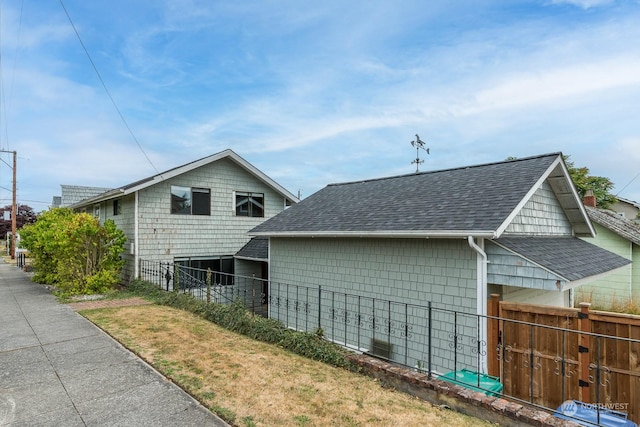 view of property exterior featuring roof with shingles and fence