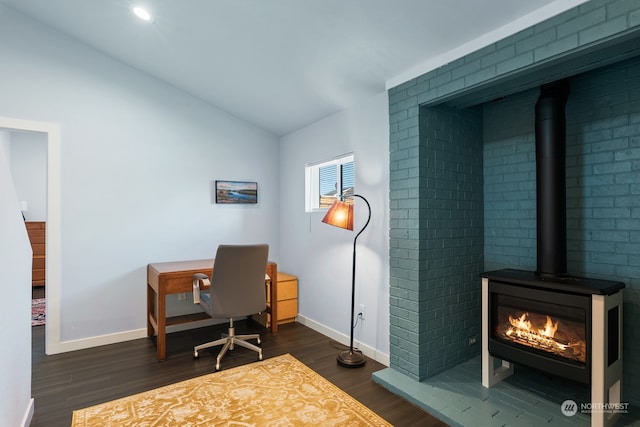 office space featuring lofted ceiling, dark wood finished floors, a wood stove, and baseboards