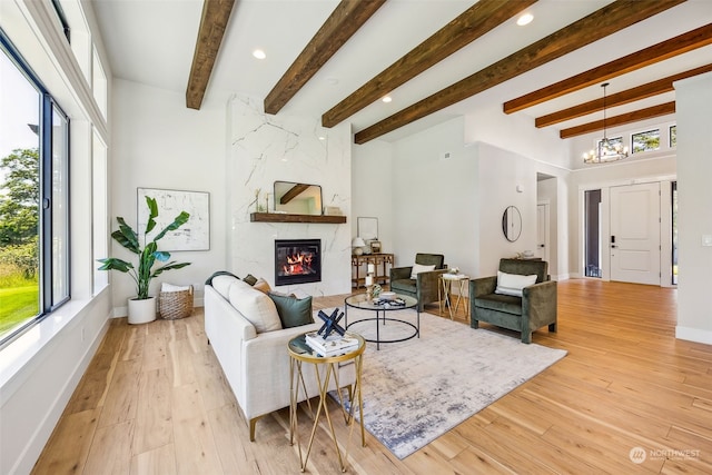 living room featuring a fireplace, an inviting chandelier, beamed ceiling, and light hardwood / wood-style floors