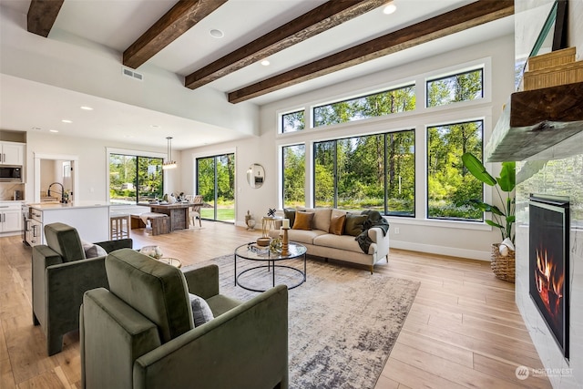 living room with light hardwood / wood-style flooring, sink, and beam ceiling