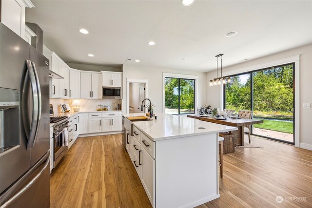 kitchen featuring stainless steel appliances, an island with sink, white cabinetry, and light hardwood / wood-style flooring