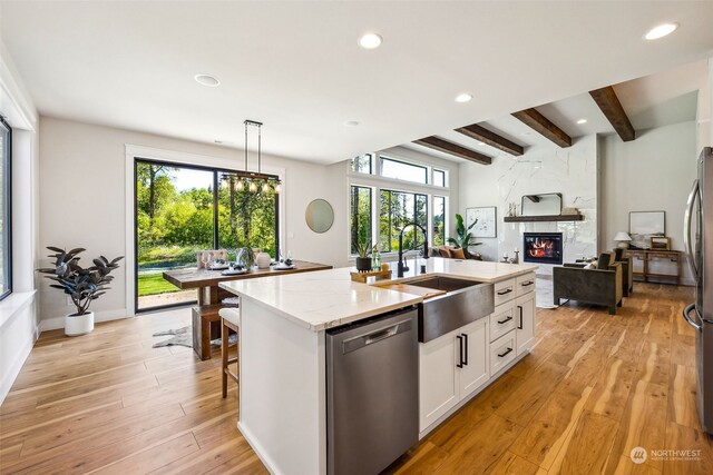 kitchen featuring a fireplace, beamed ceiling, light hardwood / wood-style flooring, a center island with sink, and stainless steel dishwasher