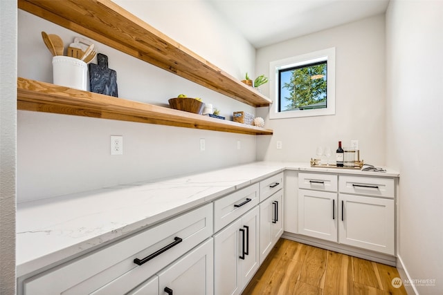 bar featuring light wood-type flooring, white cabinets, and light stone countertops