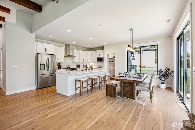 kitchen featuring wall chimney exhaust hood, appliances with stainless steel finishes, a healthy amount of sunlight, and beam ceiling