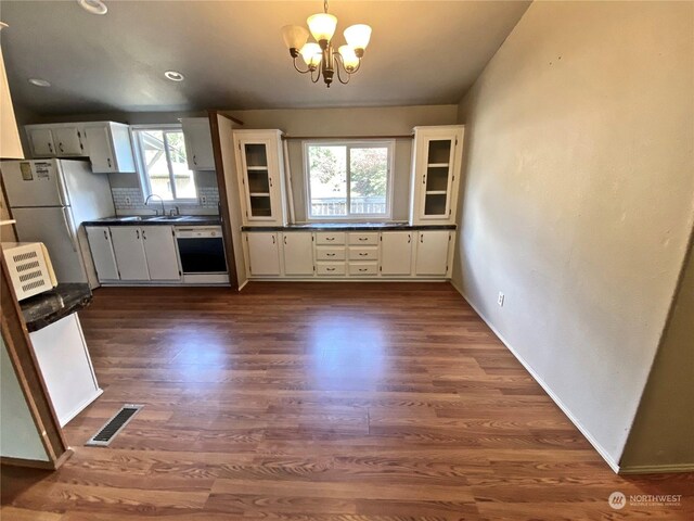 kitchen with dishwashing machine, dark wood-type flooring, visible vents, backsplash, and dark countertops