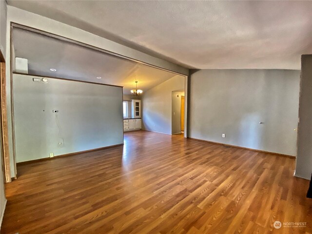 spare room with lofted ceiling with beams, baseboards, wood finished floors, and an inviting chandelier