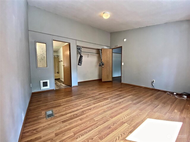 unfurnished bedroom with a closet, wood finished floors, visible vents, and connected bathroom