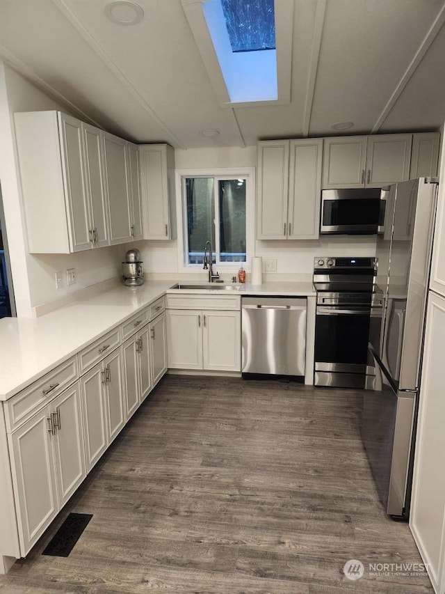 kitchen with appliances with stainless steel finishes, sink, dark wood-type flooring, and a skylight