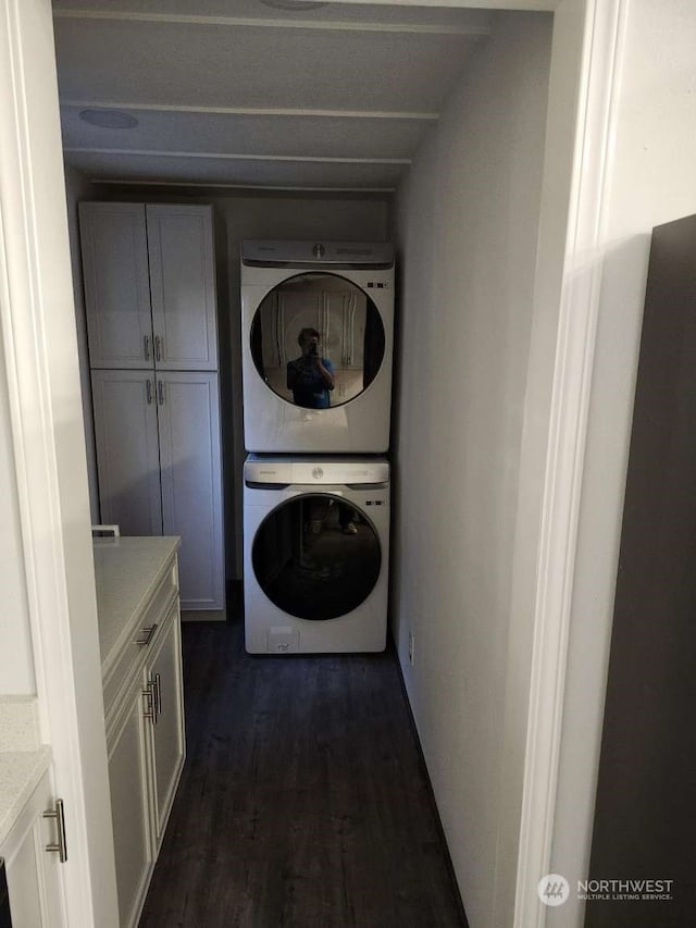 clothes washing area with cabinets, dark wood-type flooring, and stacked washing maching and dryer