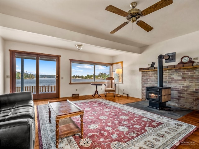 living room with ceiling fan, a wood stove, hardwood / wood-style floors, and a water view