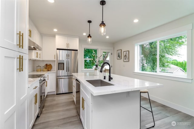 kitchen with a kitchen island with sink, a sink, white cabinets, appliances with stainless steel finishes, and decorative light fixtures