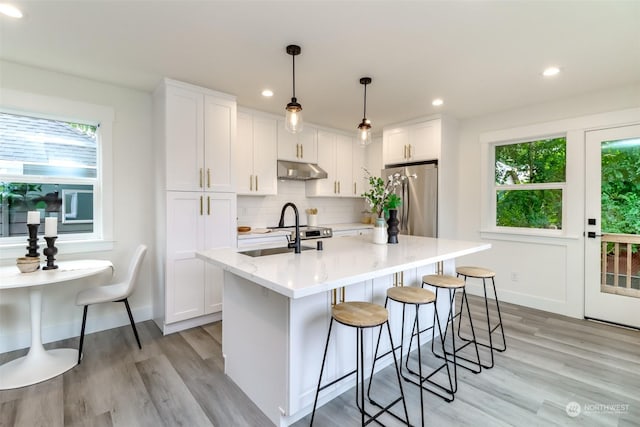 kitchen with a center island with sink, decorative light fixtures, freestanding refrigerator, light countertops, and white cabinetry