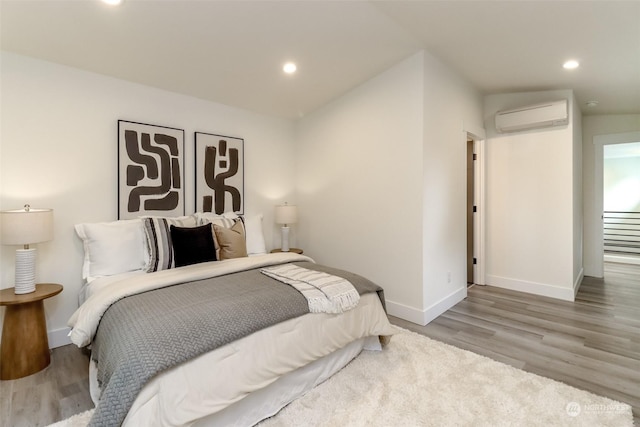 bedroom featuring recessed lighting, wood finished floors, baseboards, and a wall mounted AC