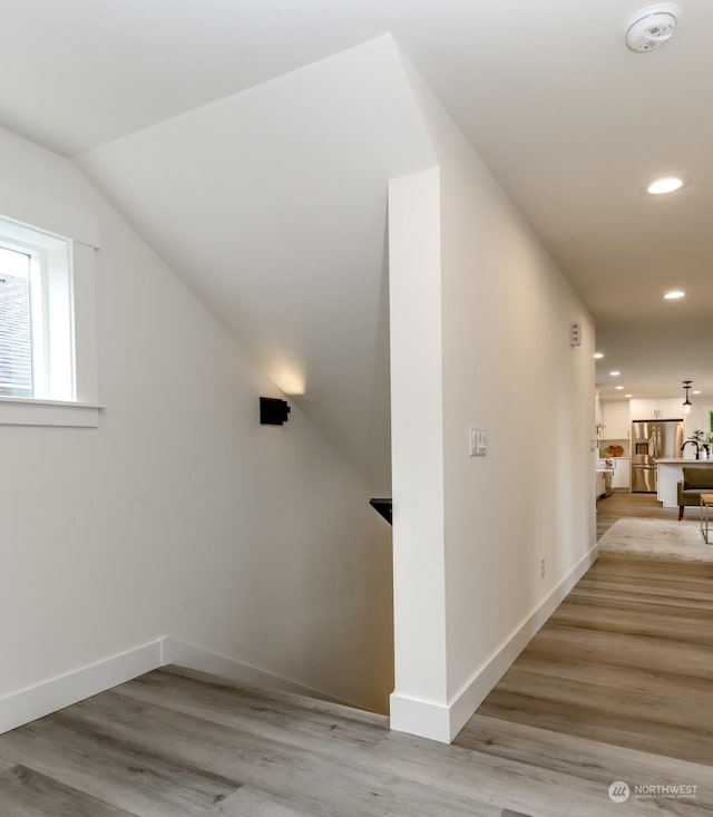 hallway with baseboards, vaulted ceiling, light wood-style flooring, and recessed lighting