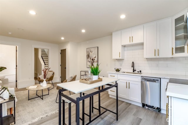 kitchen with a sink, white cabinetry, light countertops, dishwasher, and glass insert cabinets